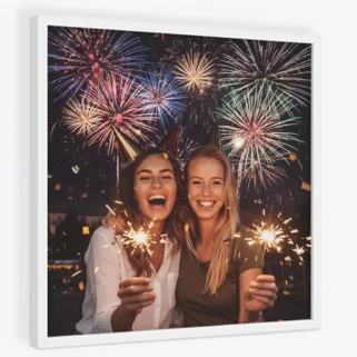 TilePix Frames New Year: A square white TilePix frame displays a photo of two smiling women celebrating with sparklers and party hats under a night sky filled with fireworks and confetti.