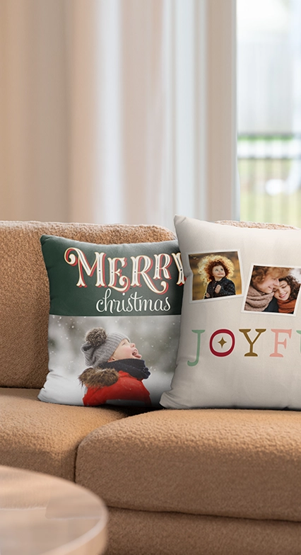 Custom Pillows: Two custom photo throw pillows resting on a tan couch; one is green with the text MERRY christmas and a photo of a child, the other is white with two photos and the text JOYFUL..