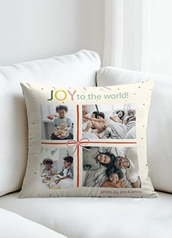 A personalized throw pillow on a white sofa featuring a four-photo collage, the text JOY to the world, and a decorative ribbon design.