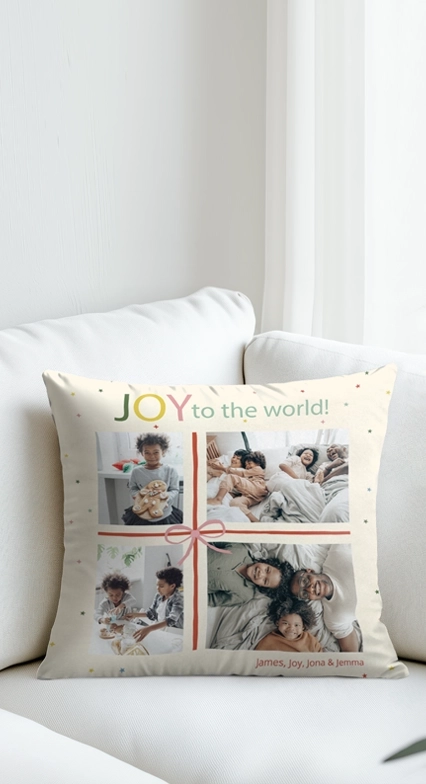 A personalized throw pillow on a white sofa featuring a four-photo collage, the text JOY to the world, and a decorative ribbon design.