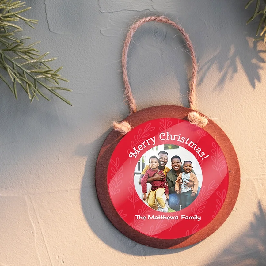Wood & acrylic ornament: A circular, wooden photo ornament with a red center that features a photo of a family of four and the white text Merry Christmas! and The Matthew's Family, hanging by a twine loop.