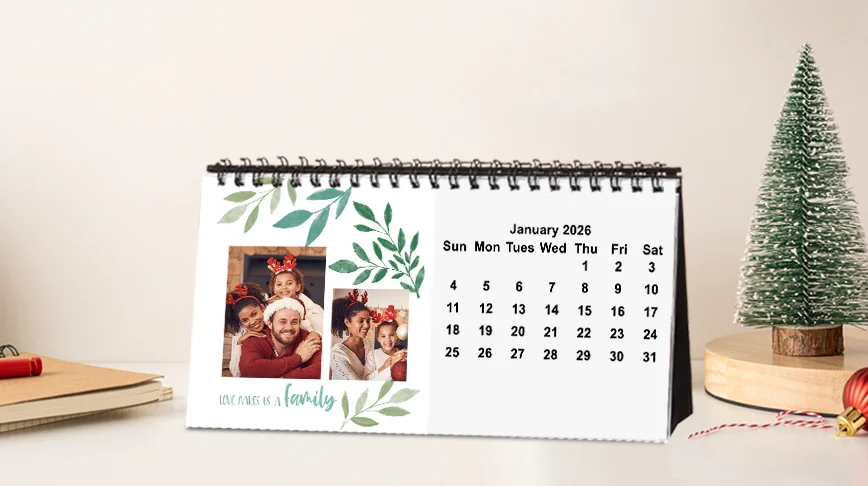 Photo desktop calendar: A spiral-bound photo desk calendar displaying the month of January 2026, with a photo collage of a family and a green leaf border design.