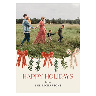A holiday card featuring a family walking in a field above a garland of red and gold bows and pine needles, with text that reads HAPPY HOLIDAYS, love, THE RICHARSONS.