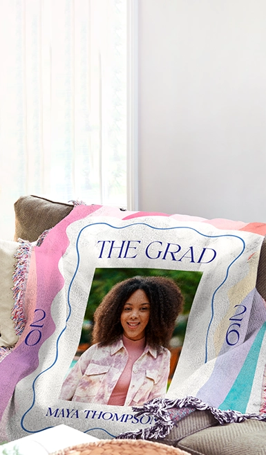 A custom photo calendar for January 20XX, featuring three smiling young girls on a pink background with bird and string light patterns, hangs on a white wall above a wooden desk with a succulent, notebooks, a pen, a mug, and a croissant.
