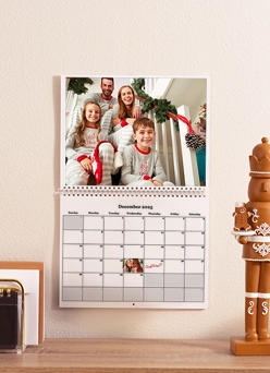 Custom Desktop Calendars: A wall calendar for December 2025 hanging above a desk, featuring a photo of a family of four smiling in matching pajamas.