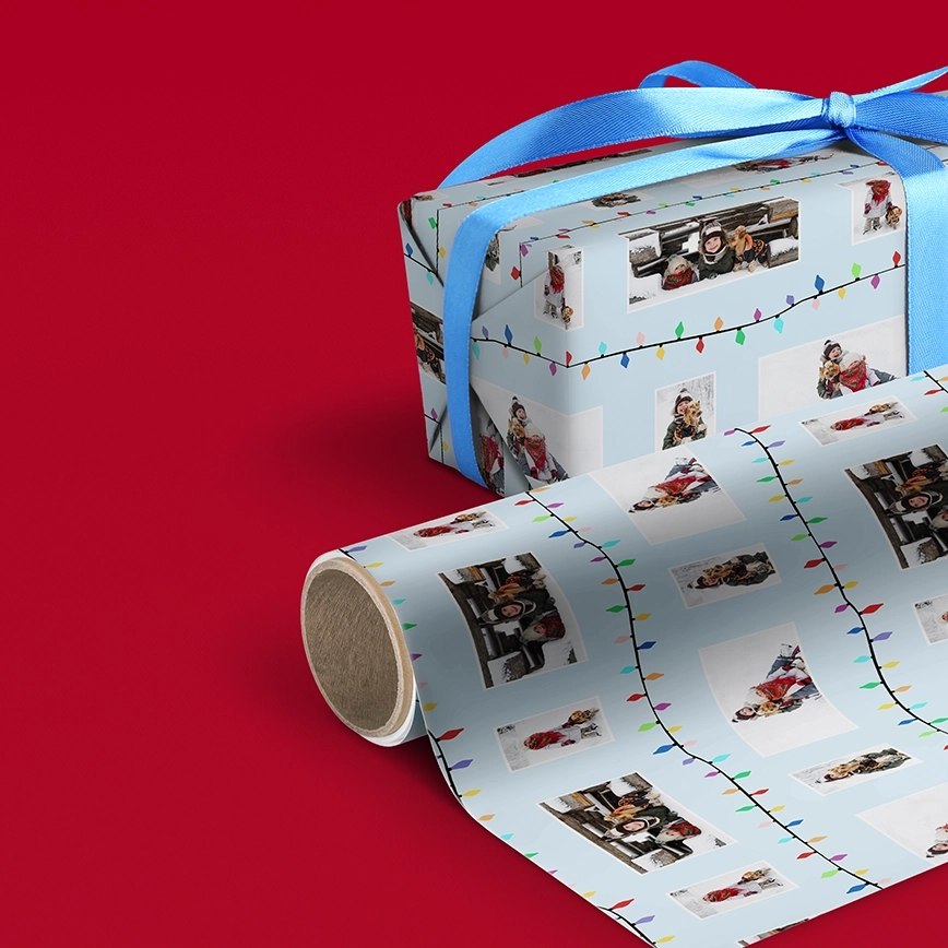Wrapping paper: Custom photo wrapping paper with a light blue background, a string light border, and multiple personalized photos, shown wrapped on a gift with a blue ribbon and next to an unwrapped roll, all set on a red surface.