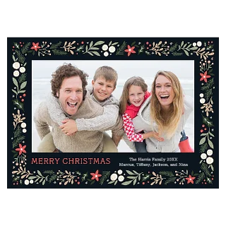 Festive Border Card 5x7: A Christmas card with a black background and a border of green leaves, white berries, and red flowers, framing a photo of a laughing family of four at the beach, with the text MERRY CHRISTMAS.